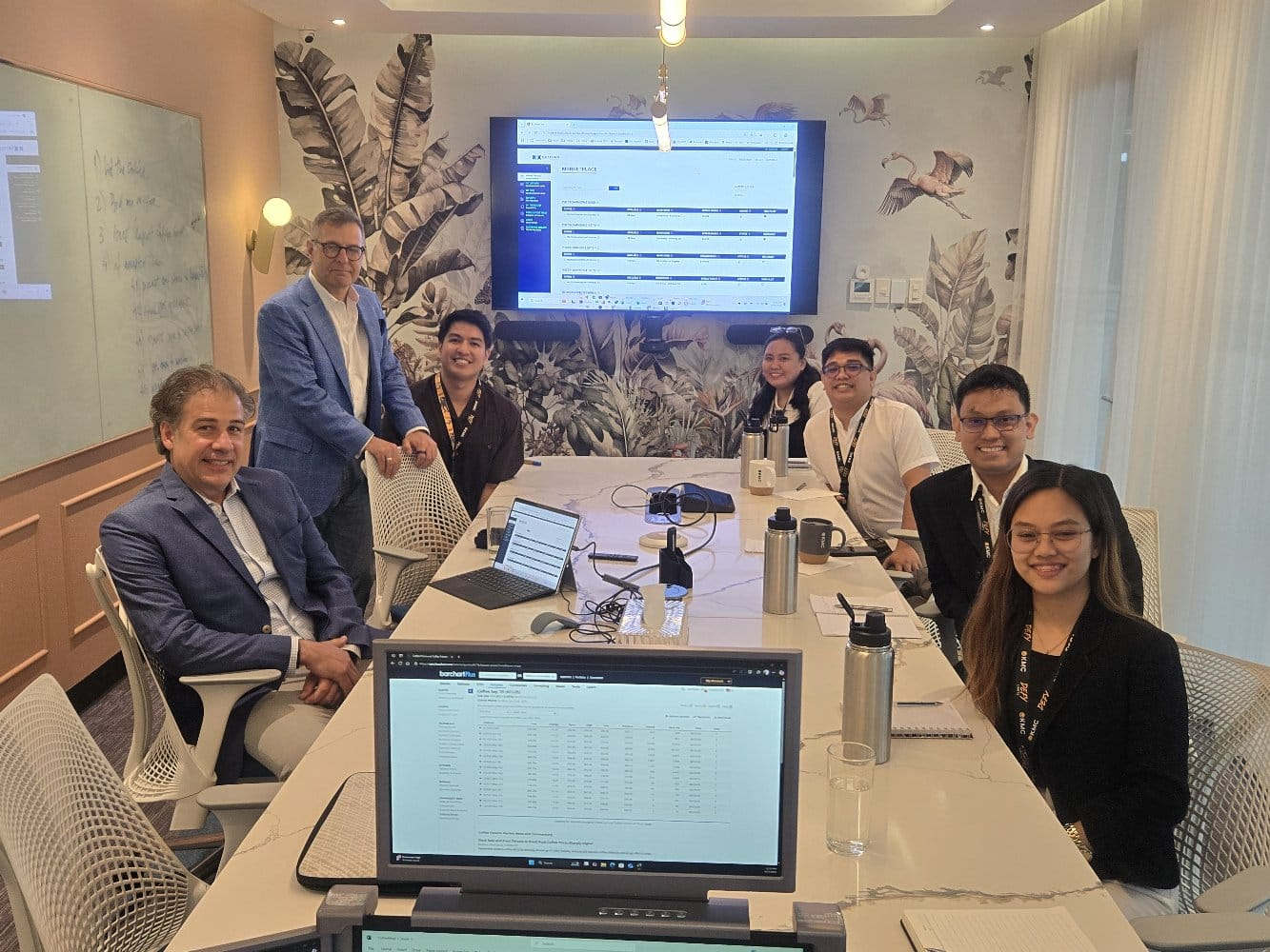 Professional team meeting in modern office with coffee trading data displays and collaborative workspace